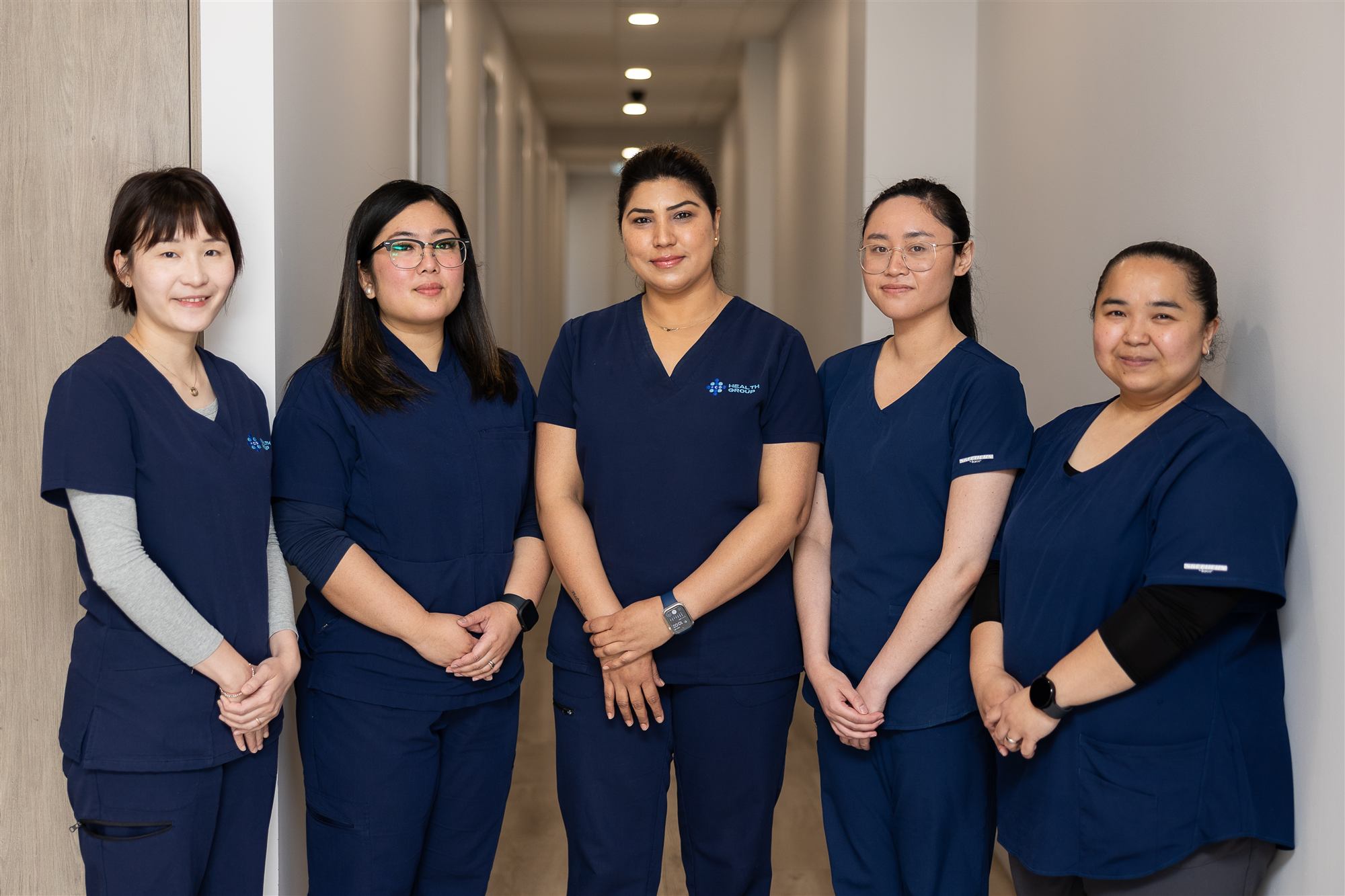 Practice nurses Elsa, Geraldine, Mamta, Celeste and Angelica standing together in the practice corridor
